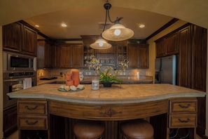 A spacious kitchen with wooden cabinets, a large island with bar stools, stainless steel appliances, and a pendant light fixture.