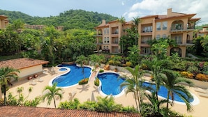 Un complejo turístico con múltiples piscinas, exuberante vegetación y montañas al fondo.
