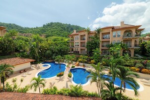 Un complejo turístico con múltiples piscinas, exuberante vegetación y montañas al fondo.