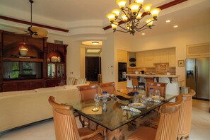 A dining area with a glass table, striped chairs, a chandelier, and a kitchen in the background. - Los Suenos Marina by Stay in Costa Rica (Jacó)