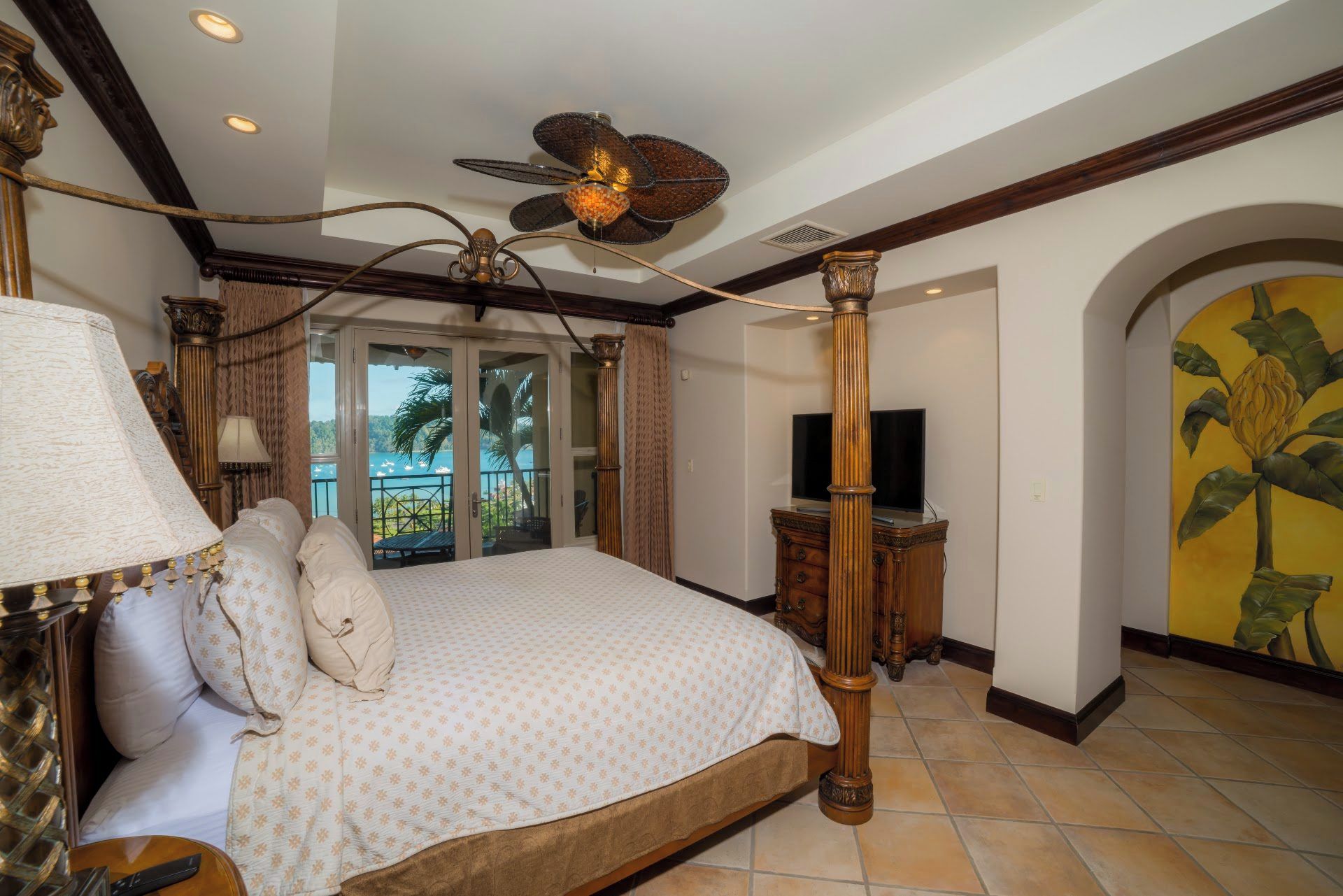 Quarto com cama de dossel, ventilador de teto, televisão e vista para o exterior através de uma porta deslizante.