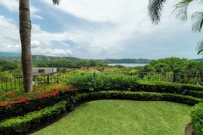 A landscaped garden with a curved pathway, palm trees, and a view of a coastal area with hills in the distance. - Los Suenos Marina by Stay in Costa Rica (Jacó)