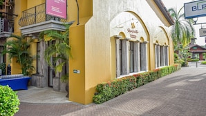 Fachada de hotel con exterior amarillo, un balcón con barandilla de hierro forjado y un cartel anunciando servicios como mostrador de turismo y alquileres vacacionales.