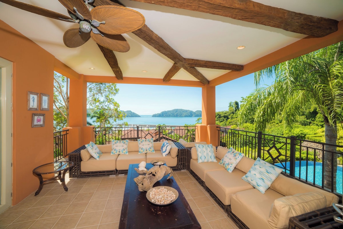 A covered outdoor seating area with a view of a body of water and mountains.