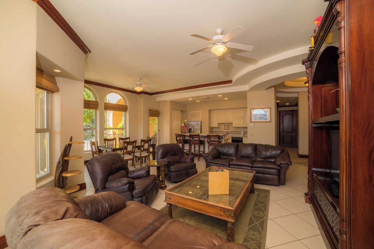 A spacious living room with leather sofas, a glass coffee table, and a ceiling fan.