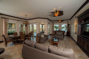 A spacious living room with a large sofa, a dining table, and chairs, a ceiling fan, and a television. - Marbella 3D 3 bdr Ocean View in Los Suenos (Jacó)