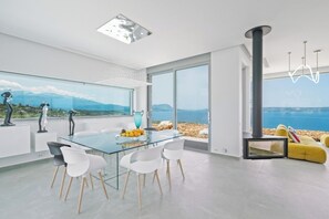 Un espace repas moderne avec une table en verre, des chaises blanches et une vue sur la mer.