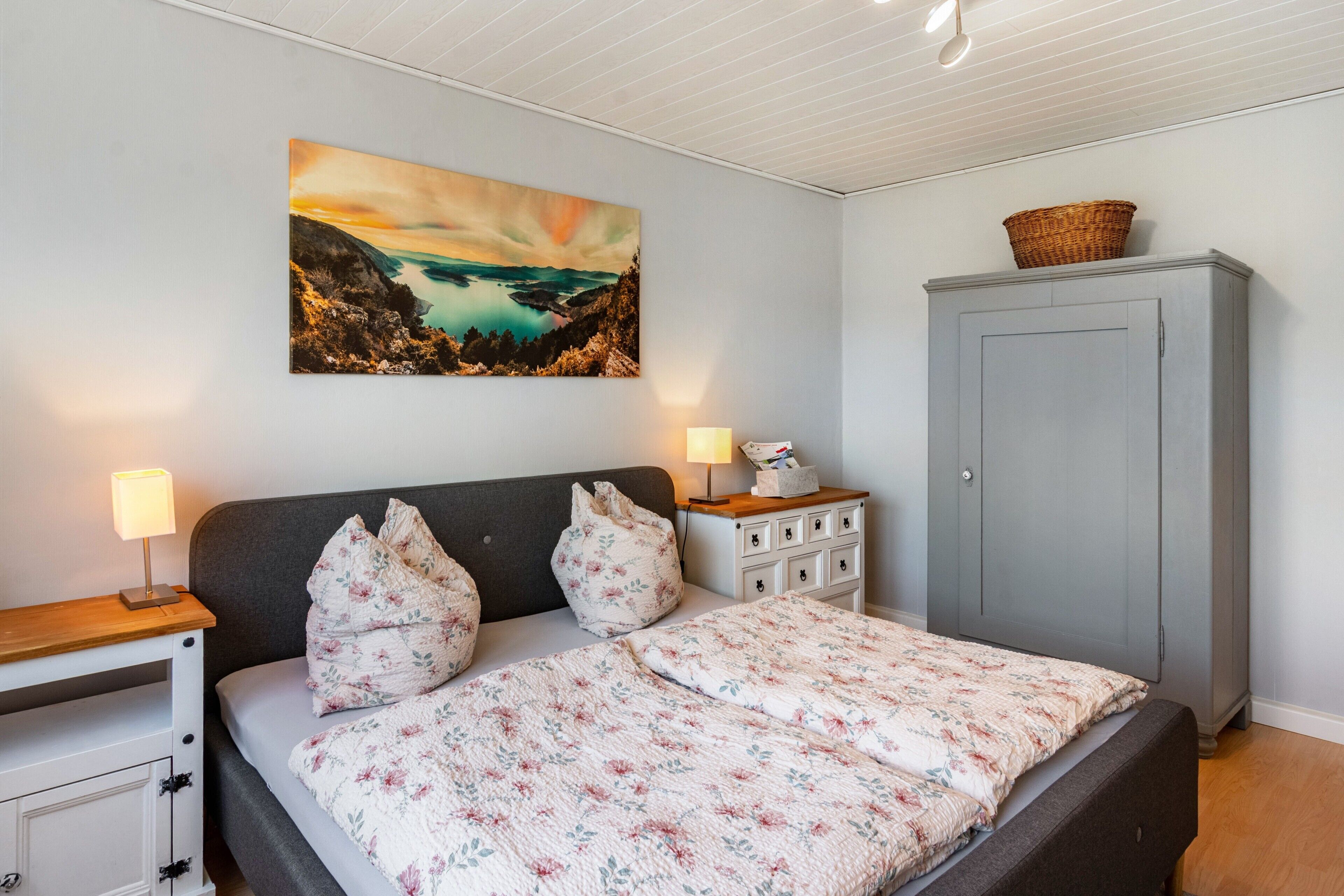 A bedroom with a bed, a nightstand, a dresser, a cabinet, and a painting on the wall.