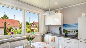 Una cocina con armarios blancos, un lavamanos y un ventanal con vistas a casas y vegetación.