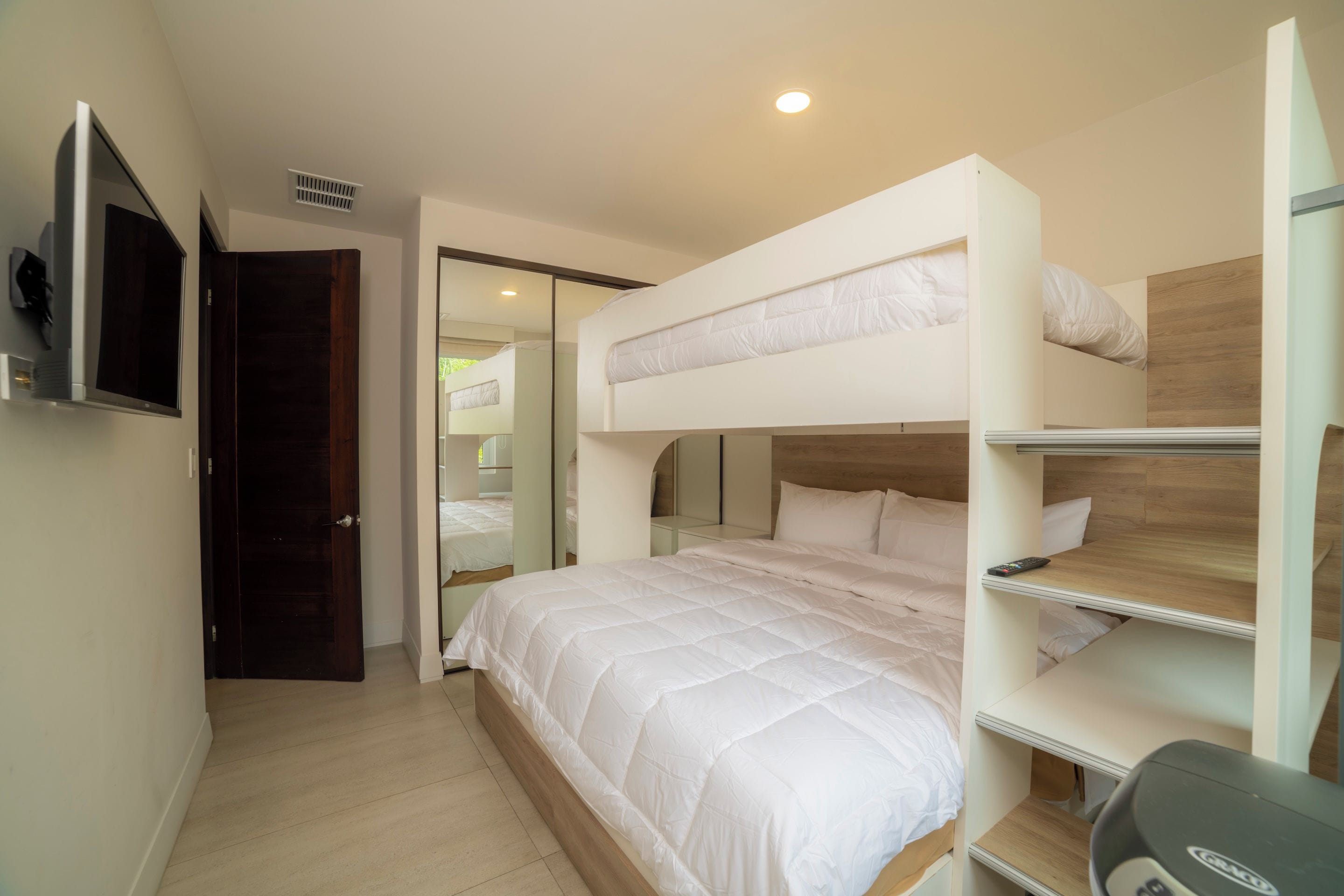 Quarto com beliche, televisão na parede, porta e espelho.