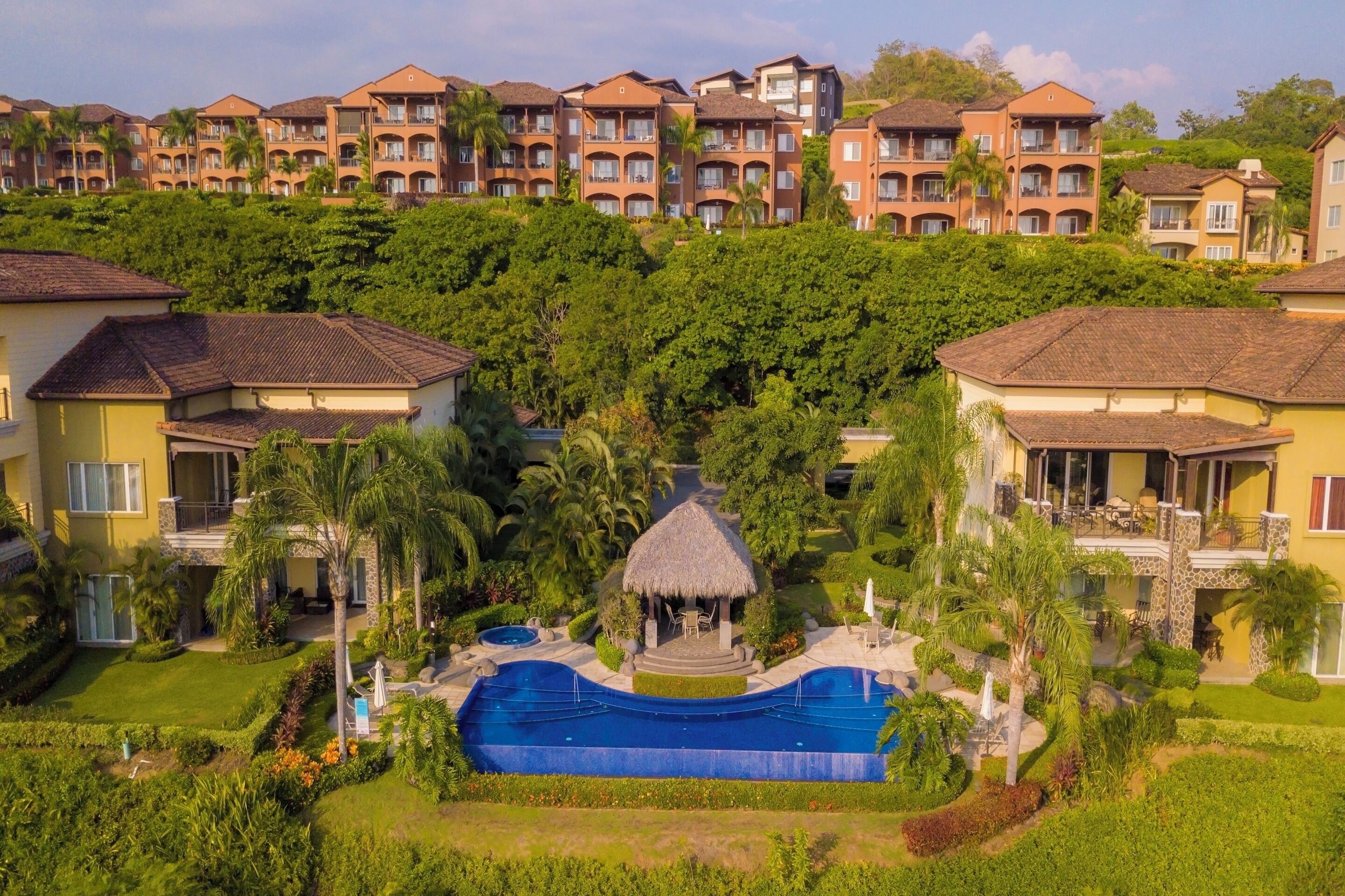 A resort with multiple-story buildings, a central swimming pool, and lush greenery.