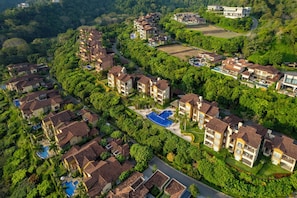 Un barrio residencial con varias casas de dos pisos, una piscina y abundante vegetación.