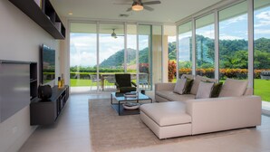 A modern living room with a large window, a sofa, a coffee table, and a television. - Vista Los Suenos by Stay in Costa Rica (Jacó)