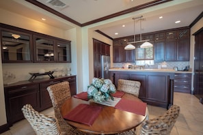 A modern kitchen with dark wood cabinets, a stainless steel refrigerator, and a dining area with wicker chairs and a wooden table. - Vista Los Suenos by Stay in Costa Rica (Jacó)
