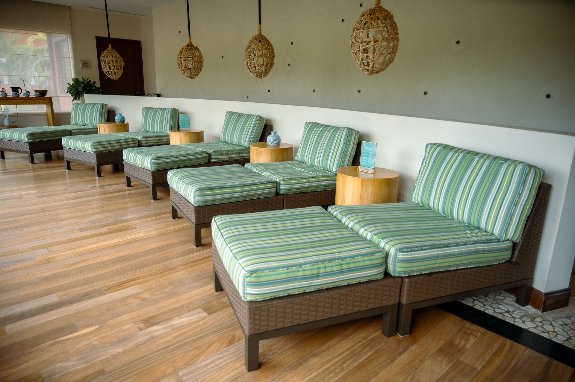 A spa room with multiple massage beds, wooden side tables, and woven pendant lights.