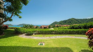 A well-maintained garden with a stone pathway, neatly trimmed hedges, and a view of the sea and hills in the background. - Vista Los Suenos by Stay in Costa Rica (Jacó)