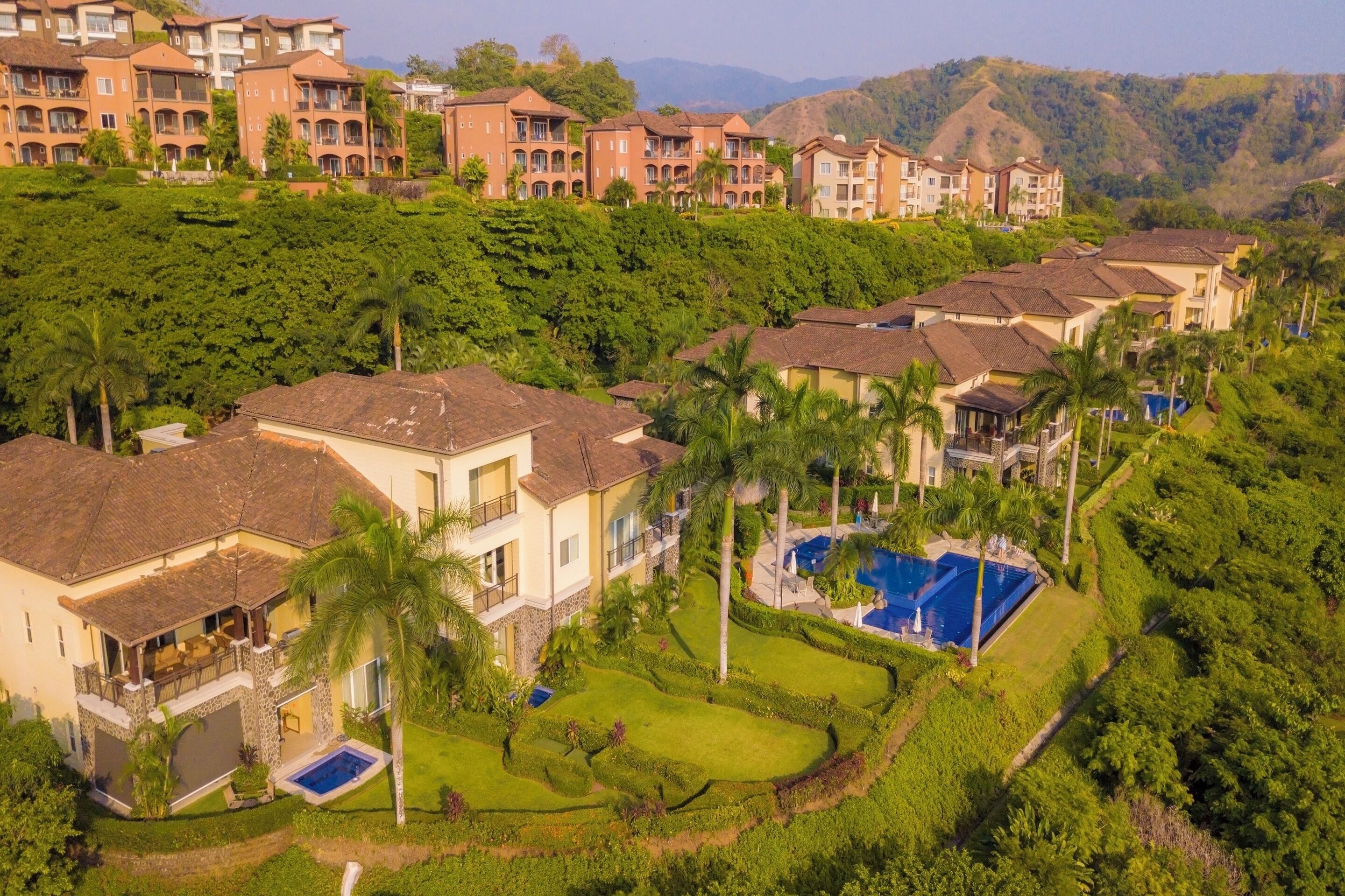 Zona residencial con varias casas de dos pisos, una piscina y abundante vegetación.