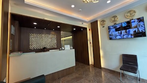 A reception area with a modern design, including a reception desk, a wall-mounted TV displaying security footage, and a decorative ceiling light. - Hotel Downtown-Near US Embassy (Mumbai)
