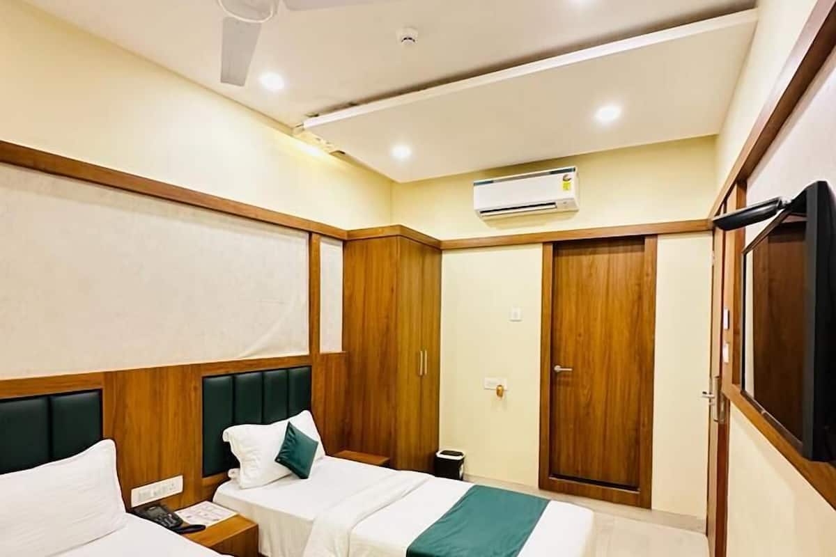 Quarto de hotel com duas camas, um ventilador de teto, ar condicionado e guarda-roupas de madeira.
