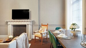 A dining area with a fireplace, a television above it, and a table set for four with chairs. - Hertford Flat 7 (London)