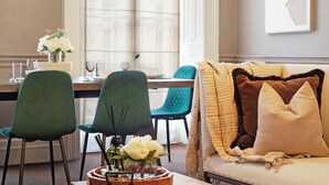 A dining area with a table set for two, two green chairs, and a vase with white flowers. - Hertford Flat 7 (London)