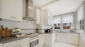 A modern kitchen with white cabinets, a stainless steel range hood, and a granite countertop. - Hertford Flat 8 (London)