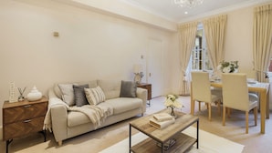 A living room with a sofa, coffee table, and dining area with chairs and a table. - Hertford Flat 8 (London)