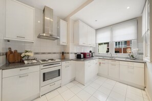 Una cocina moderna con armarios blancos, campana de acero inoxidable, horno empotrado y encimera de granito.