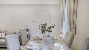 A dining area with a white table set for four, surrounded by chairs, with a vase of flowers on the table. - Hertford Flat 8 (London)