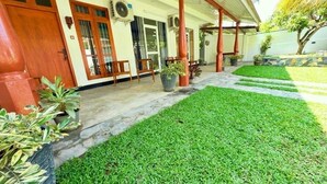 Un edificio con porche cubierto, césped cuidado y varias plantas en macetas.
