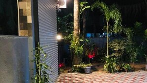 Un espacio al aire libre empedrado con suelo de baldosas estampadas, rodeado de plantas diversas y una palmera.