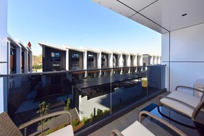 Un bâtiment moderne doté d’un balcon en verre, de meubles en osier et offrant une vue dégagée sur les immeubles voisins.