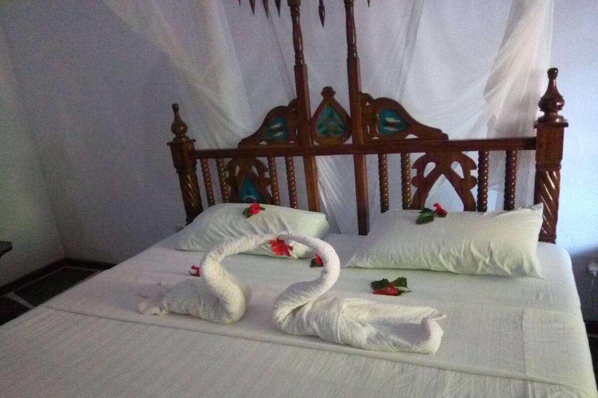 A bed with a wooden headboard, white bedding, and decorative swans made of towels with flowers.
