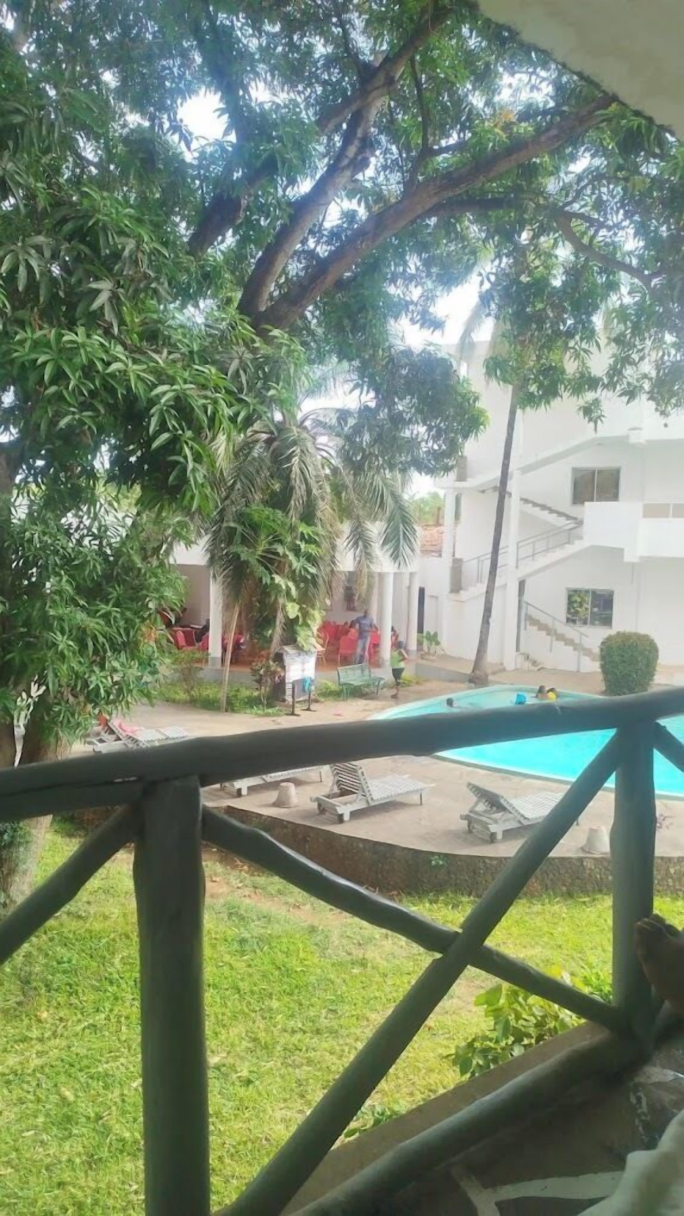 Ein Poolbereich mit Liegestühlen und einer kleinen Terrasse, umgeben von Grünflächen und einem Gebäude mit einer Treppe.