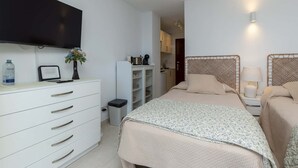 A bedroom with a bed, bedside tables, a TV, a wardrobe, and a small kitchenette. - Ocean View 3 (Los Cristianos)