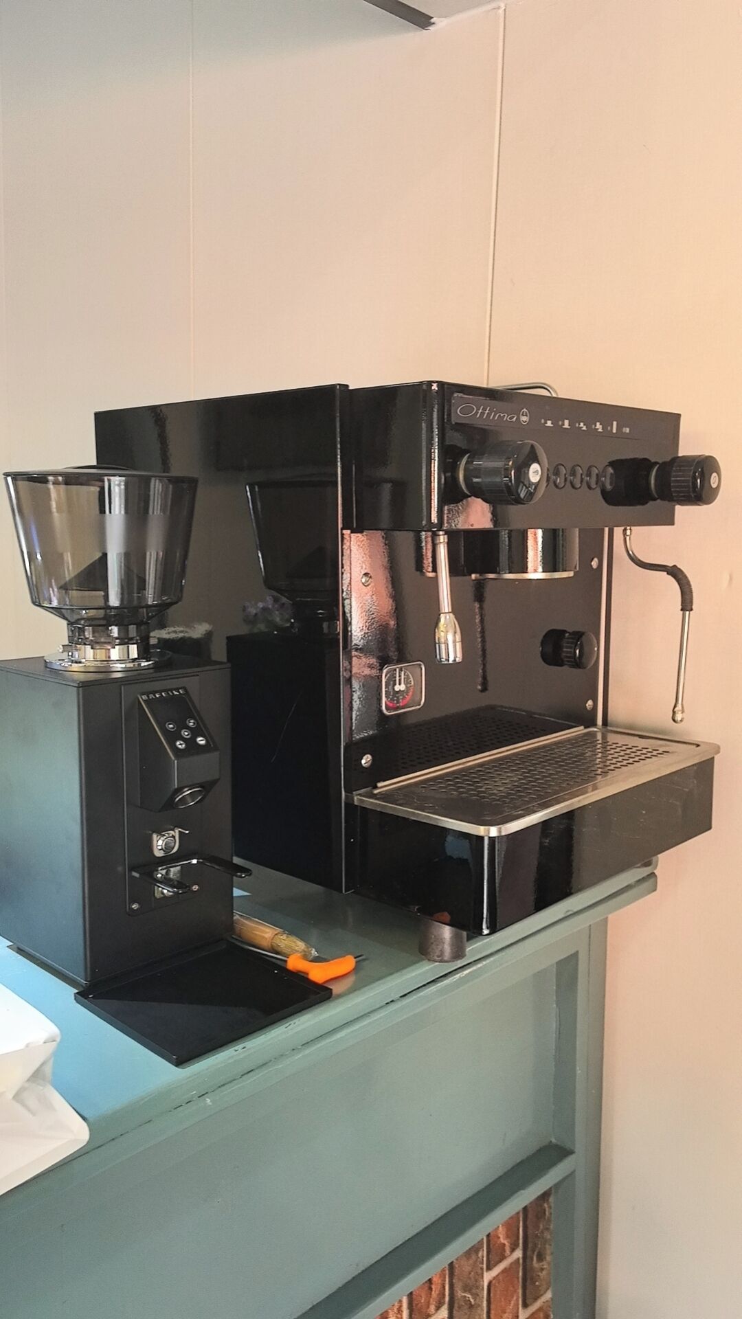 A black espresso machine with a digital display, a portafilter, and a drip tray on a teal counter.
