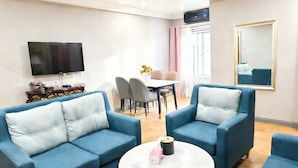 A modern living room with two blue sofas, a round coffee table, a flat-screen TV, a dining area with a table and chairs, and a large mirror on the wall. - JUN YUE GRA Lagos hotel (Lagos)