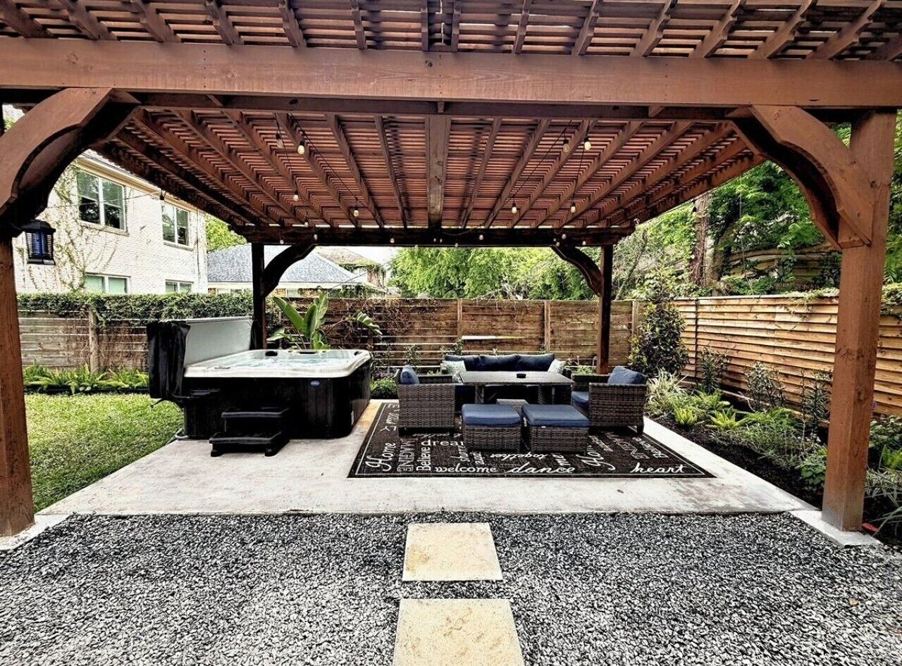 Un patio techado con mobiliario exterior, incluyendo una mesa y sillas, y un jacuzzi.