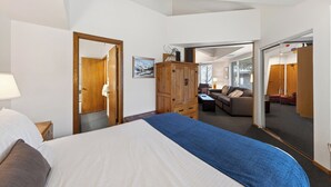 Habitación de hotel con cama, armario de madera y un espejo que refleja una sala de estar con sofá y sillones.