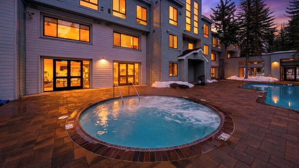 Un edificio de varios pisos con piscina, iluminación exterior y nieve en el suelo.