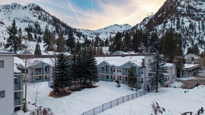 Un centro turístico montañoso cubierto de nieve, con edificios de varios pisos, un telesilla y cielo despejado.
