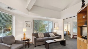 Una sala de estar moderna con un sofá gris, un sillón gris, una mesita de centro y un televisor sobre un mueble de madera.