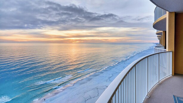 Un balcon doté d’une balustrade incurvée, donnant sur une plage au coucher du soleil.