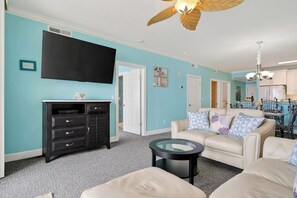 Ein Wohnzimmer mit einer türkisfarbenen Wand, einer schwarzen Unterhaltungseinheit, einem beigefarbenen Sofa und einem Deckenventilator.