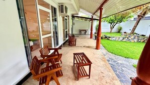 An outdoor patio with wooden furniture, a covered area, and a well-maintained lawn. - Devon Surf  Inn : Deluxe Double Room (Dikwella)