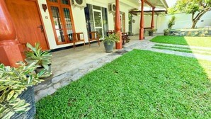 A building with a covered porch, a well-maintained lawn, and potted plants. - Devon Surf  Inn : Deluxe Double Room (Dikwella)