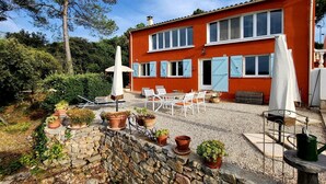 Ein zweigeschossiges Haus mit roter Fassade, einer Terrasse mit Gartenmöbeln und Blumentöpfen.