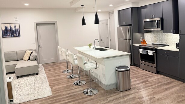 Una cocina moderna con una isla central, electrodomésticos de acero inoxidable y una zona de estar con sofá y taburetes de bar.