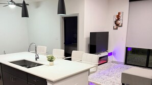 Una cocina moderna con una isla central, un área de comedor con un sofá blanco y un televisor de pantalla plana.