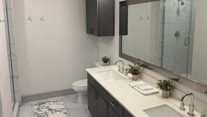 Un baño moderno con un espejo grande, dos lavamanos, un inodoro y una zona de ducha.